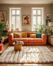 Cozy living room with Moroccan wool rug, an orange sofa, colorful cushions, and a wooden coffee table.