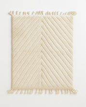 Beige textured rug with diagonal pattern and tassels on a white background