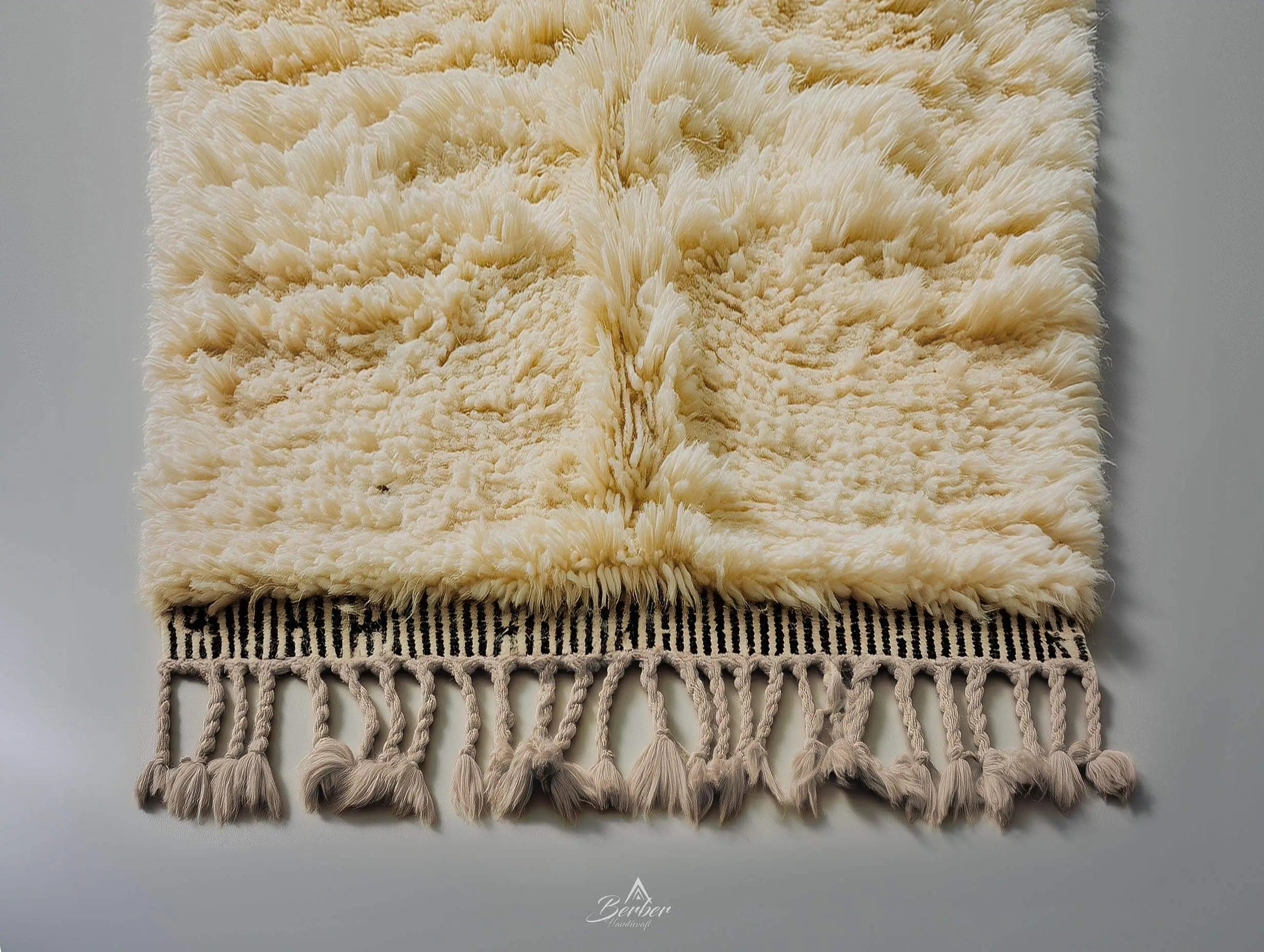 Beige textured berber rug with tassels on a gray background