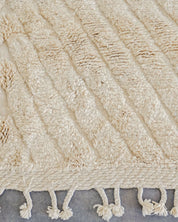Close-up of a textured beige rug with tassels on a gray background