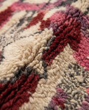 Close-up of a textured rug with red, beige, and purple patterns