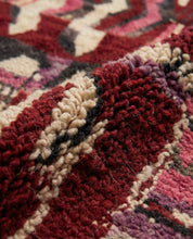 Close-up of a textured rug with red, beige, and purple patterns