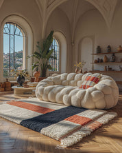 Modern living room with a white sofa, coffee table, orange and white moroccan rug, and decorative elements.
