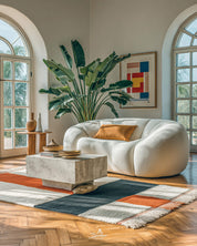Modern living room with a white sofa, coffee table, orange and white moroccan rug, and decorative elements.