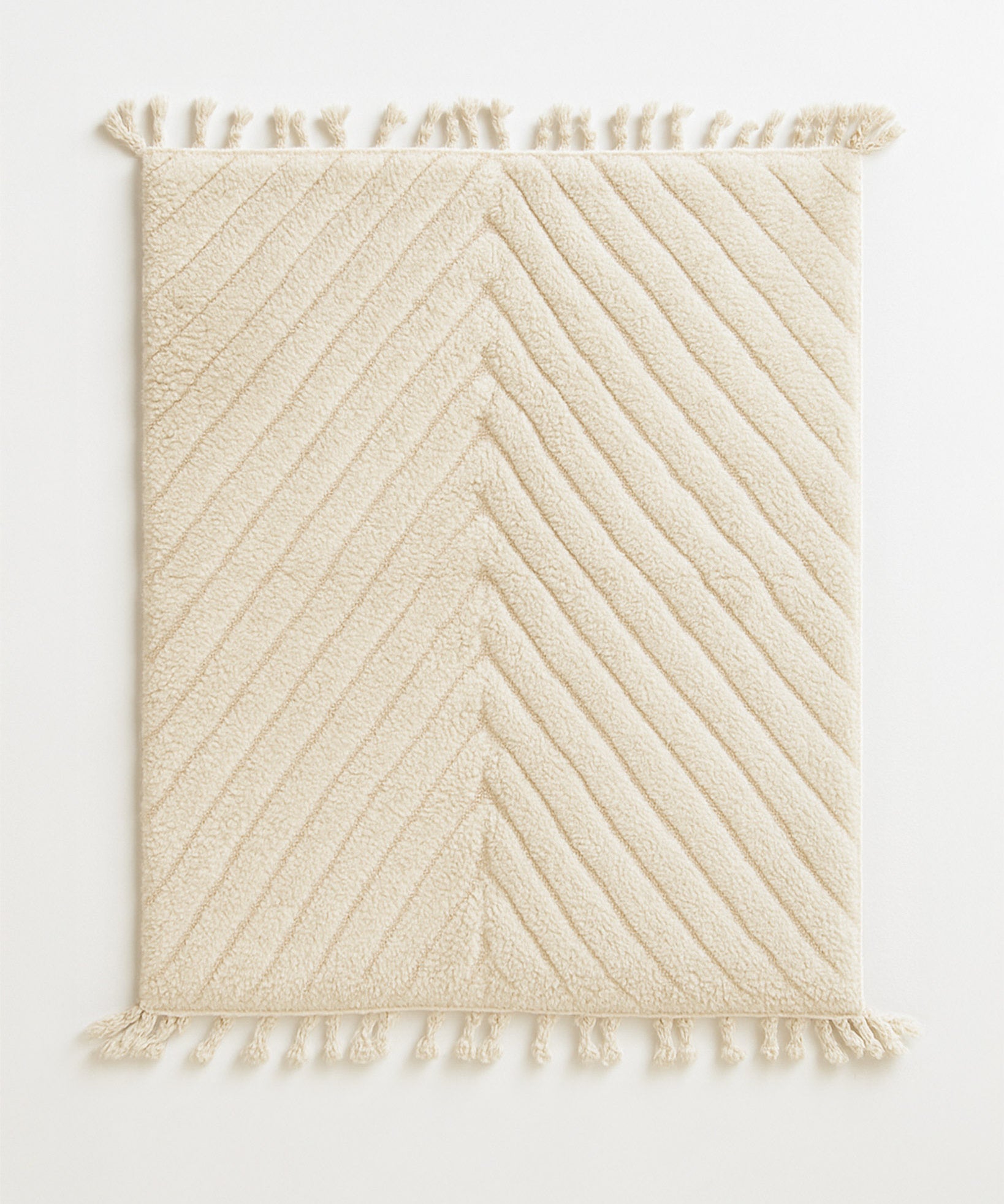 Beige textured rug with diagonal pattern and tassels on a white background