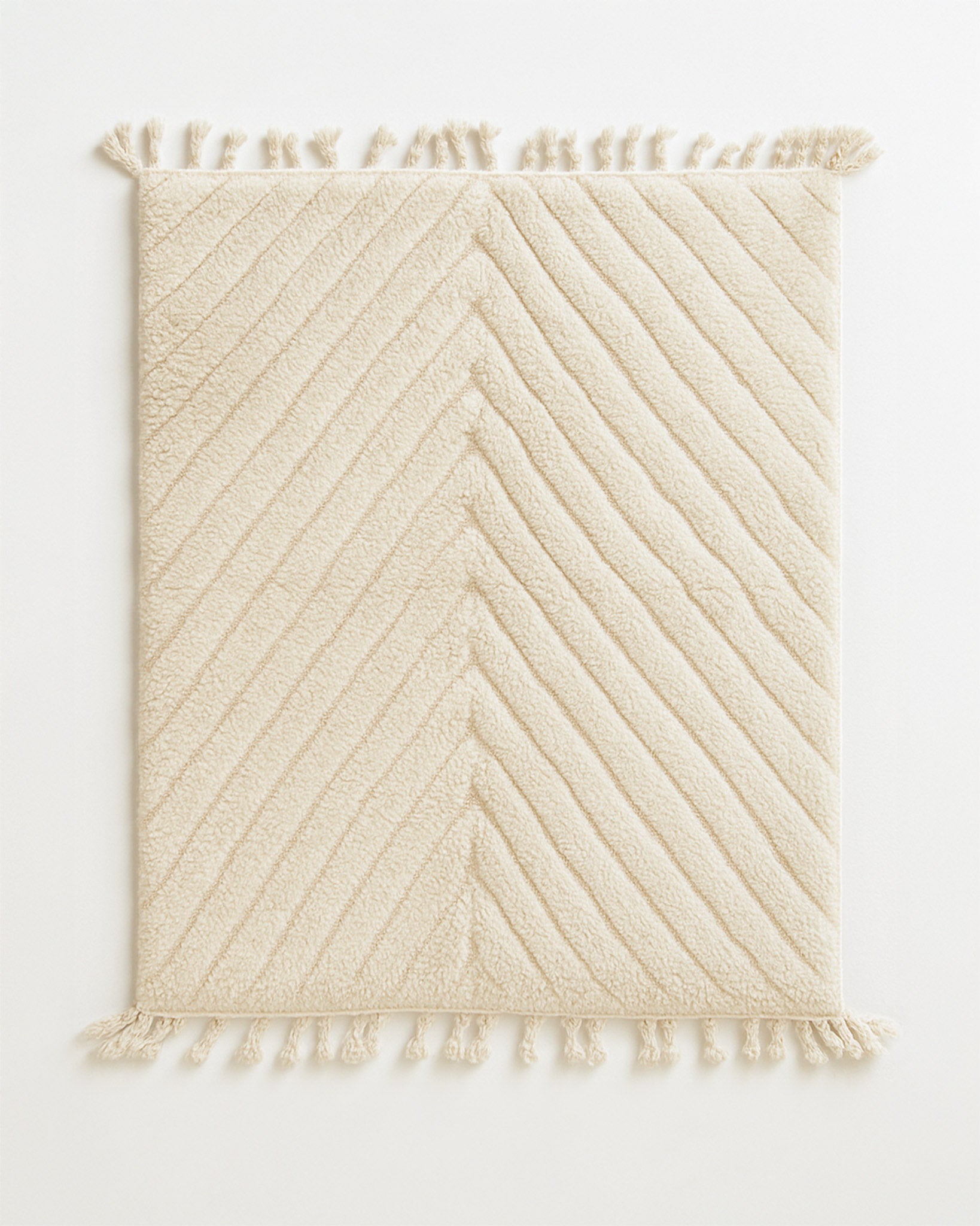 Beige textured rug with diagonal pattern and tassels on a white background